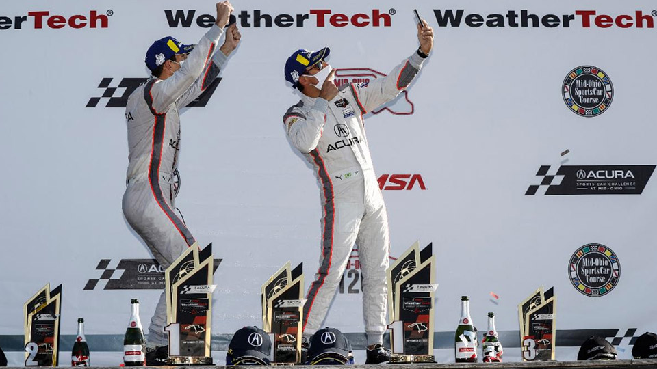 Ricky Taylor and Helio Castroneves pose for a selfie atop the stage at Mid-Ohio Sports Car Course